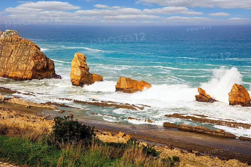 Storm waves break on the coastal rocks. Snow-white sea foam glistens in the dim autumn sun. Playa de la Arnia beach. Cantabria, Spain. Amazing geological formations amaze tourists
