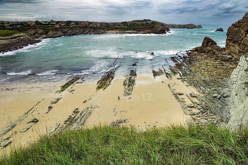 Giant rough gray rocks and smooth sandy beach. Noon on the beach of Playa di Arnia, Spain. Rocky picturesque ocean coast. Cantabria. Windy stormy day on the Atlantic coast
