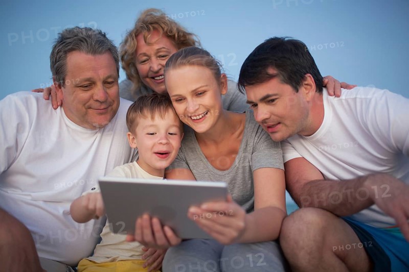 Happy big family having good time together. Grandparents and parents looking at the pad screen while boy using it