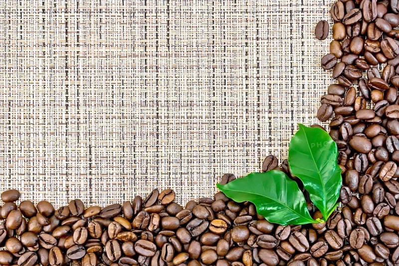 Frame of black coffee beans with leaves on brown coarse woven fabric