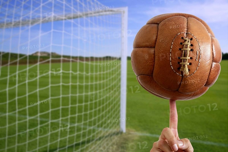 Football vintage ball in hand net soccer goal green grass background