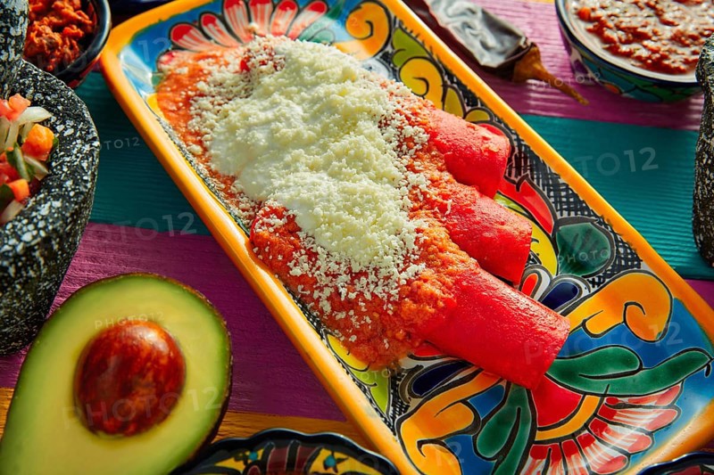 Red enchiladas Mexican food with guacamole and sauces on colorful table
