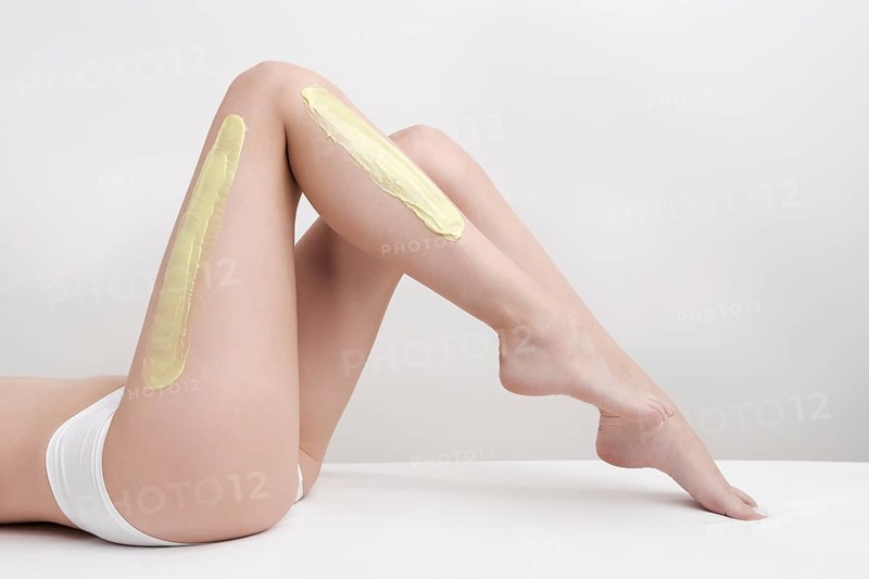 Beautiful woman legs while she lying down on couch during depilation process with green hot wax in professional beauty salon. Side view of slim young women body in white panties. Part of photo series