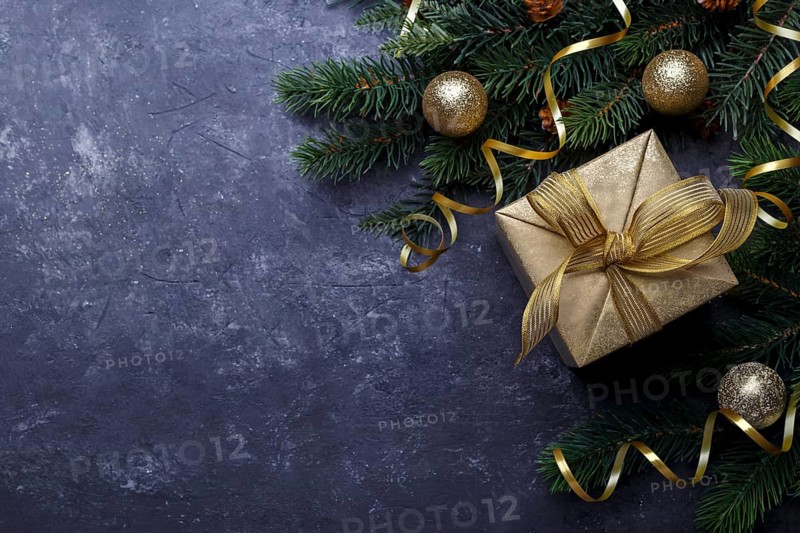 Christmas flat lay with golden gift box and fir tree branch on black stone background with copy space