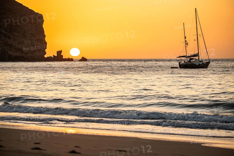 Sunrise during a storm, Calima. A haze-covered horizon turns orange as the sun rises as a ball. A boat is anchored in the sea. Landscape photograph in Gran Tarajal, Canary Islands, Spain, Europe