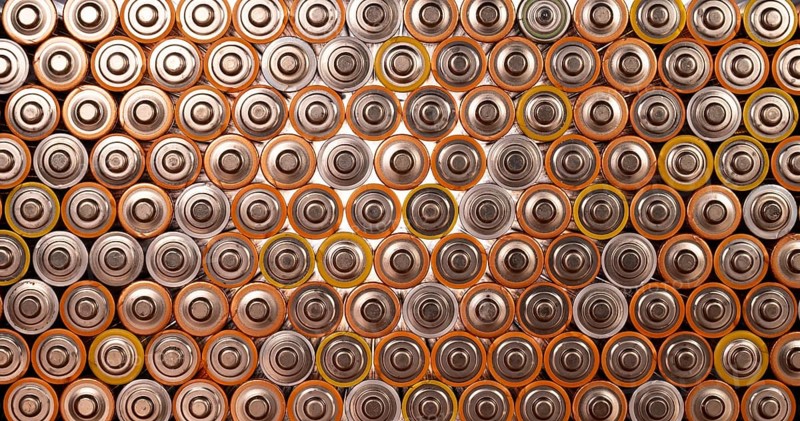 Multiple used AA alkaline batteries are seen arranged in a pile. Closeup front view from the plus side of the battery