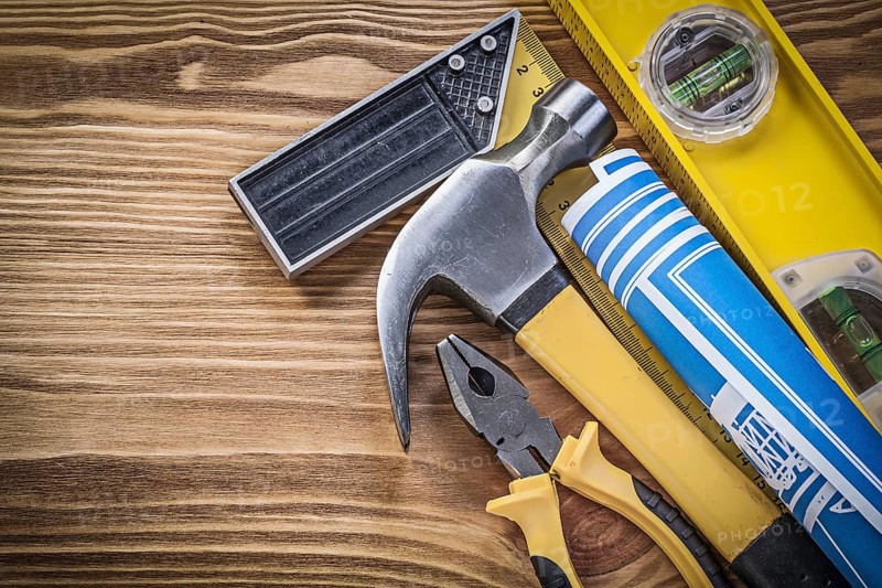 Blue blueprints construction level try square claw hammer pliers on wooden board
