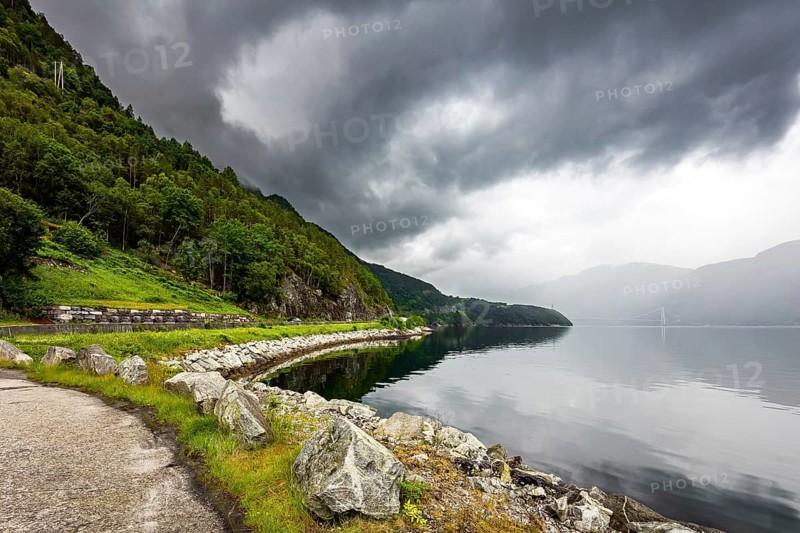 Scenic road in the mountains of Western Norway. Beginning of the Hardangerfjord. Scandinavia. Summer. Powerful clouds are reflected in the water surface of the fjord