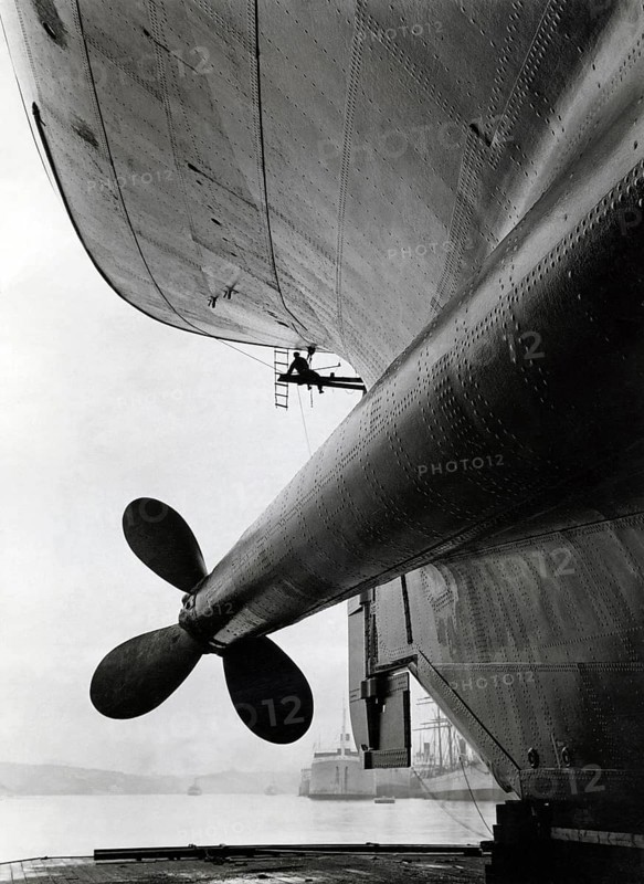 Dockyard in the 1930s. The ship M/S Gripsholm is undergoing maintance and the ship is risen in a dry dock. One of the stern propellers is visible and a worker is seen working on the hull. Theh ship was delivered 1925 to the swedish shipping company Svenska Amerika Linien and was at the time the most moderna ship on the Atlantic. It had a length of 168, 5 meter and 22, 7 meter wide. A veritble luxury palace in witch the most famous people travelled the seas. It was built in Newcaste England by Armstrong, Whitworth & Co