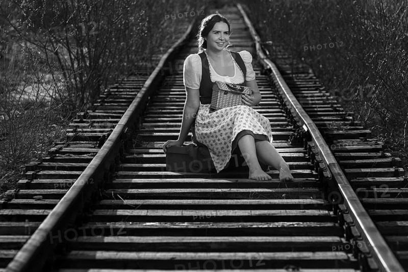 Woman in traditional dirndls sits on railway tracks, relaxed and smiling, black and white picture, Mindelheim, Unterallgäu, Bavaria, Germany, Europe