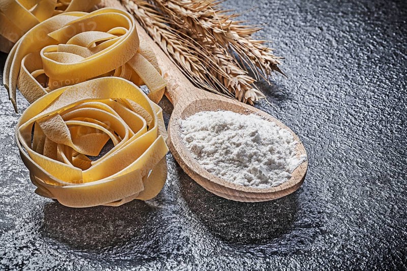 Wheat rye ears wooden spoon flour raw twisted Italian pasta on black background