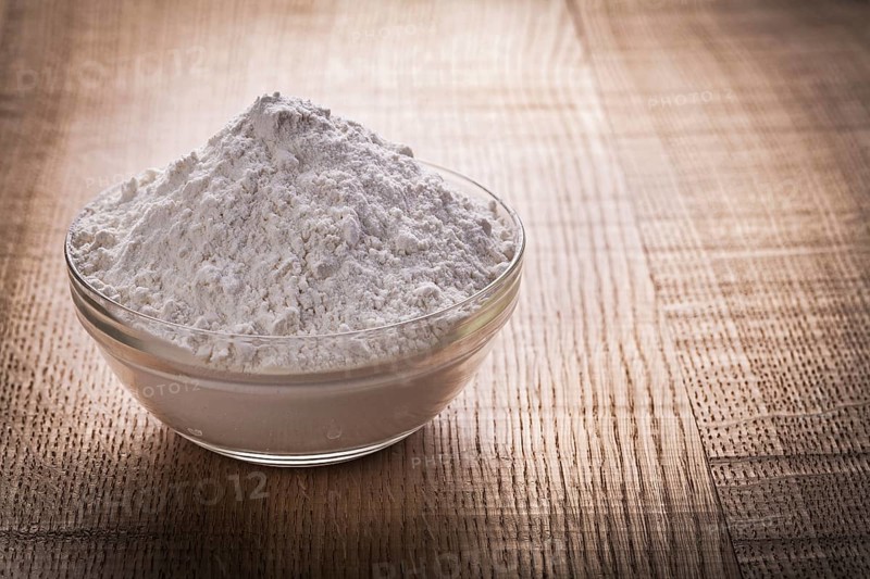 Transparent glass bowl with white natural flour on vintage wooden board food and drink still life