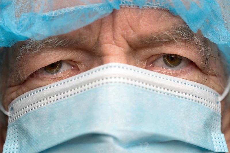 Close up portrait of sad senior adult dressed in surgical face mask with ear straps, covering nose from SARS, virulently infectious disease corona virus. Sad gaze man eyes during pandemic, quarantine
