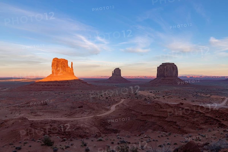 A picture of the Monument Valley landscape at sunset, with the West Mitten Butte, East Mitten Butte and Merrick Butte rock formations in the center