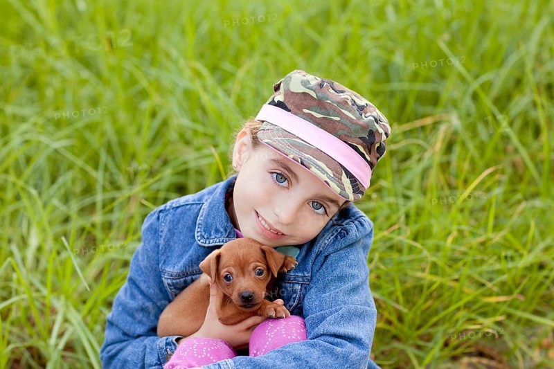 Little girl with pet puppy mascot mini pinscher in outdoor green grass