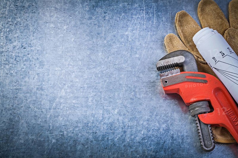 Monkey adjustable wrench protective gloves rolled blueprints on metallic background plumbing concept