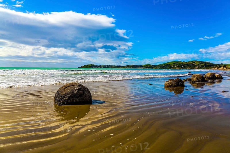 Moeraki's huge round boulders on a sandy beach. The Pacific ocean tide begins in New Zealand. The sun's rays are reflected in the ocean water. The concept of ecological, exotic and phototourism