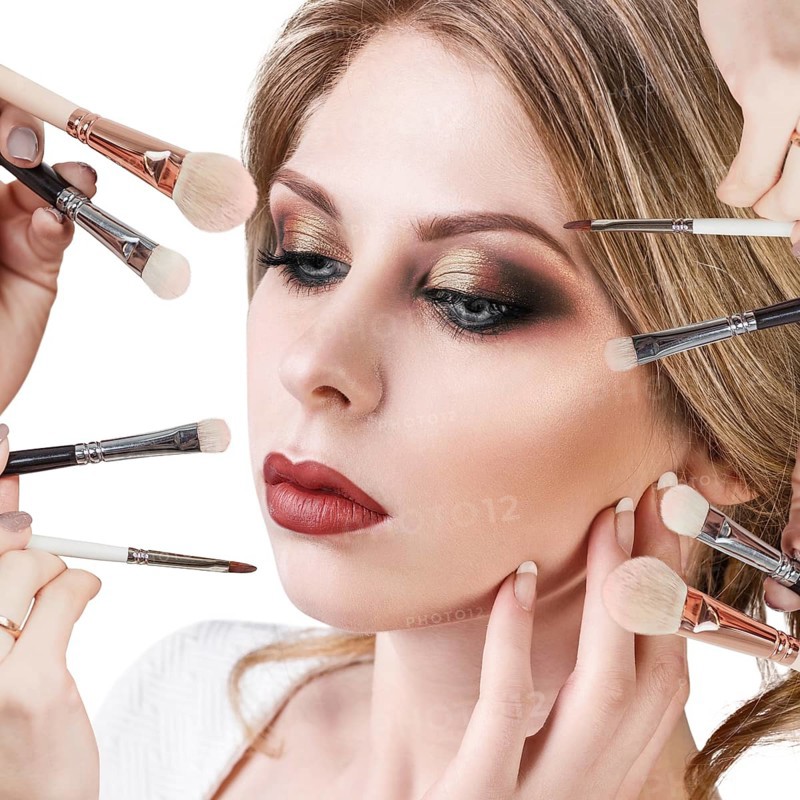 Many hands with cosmetics brushes applying make-up to glamour woman