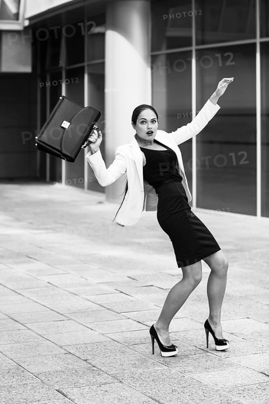 Scared young businesswoman with briefcase and gesturing fear on city background