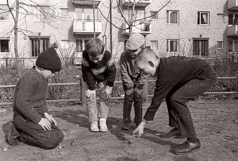 In the 1960s. Boys outdoors playing marbles. An old fashioned game where the goal is to hit the pyramid of marbles with just one marble. If you hit, you won the marbles in the pyramid, otherwise the marble was lost. There was also variants of the game. Sweden spring 1964. Roland Palm ref pärm 2
