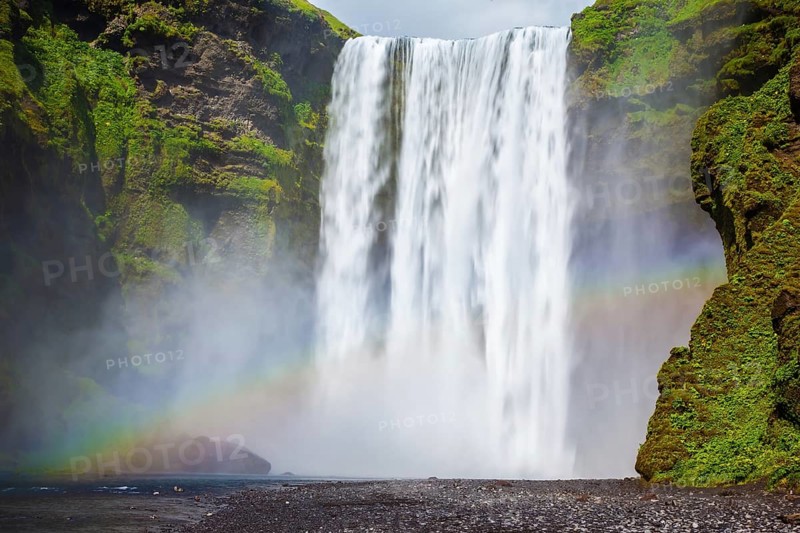 Picturesque rainbow appears in the water mist. The most popular waterfall in Iceland - Skogafoss. Water rushes down with a crash, forming a cloud of mist