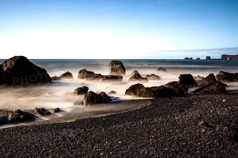 Rocks by the sea with foaming waves under a clear blue sky, Iceland, Europe