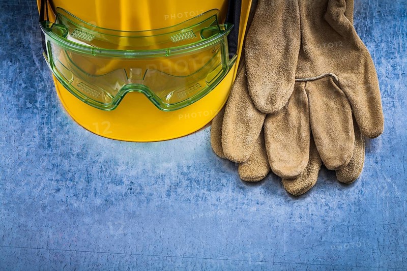 Safety leather gloves hard hat and multiple-purpose protective glasses on scratched metallic background construction concept