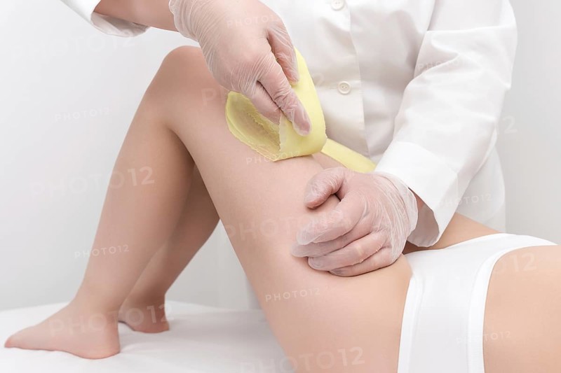 Cosmetologist hands in gloves removing hair on women leg. Depilation procedure with green hot wax in professional beauty salon. Part of photo series