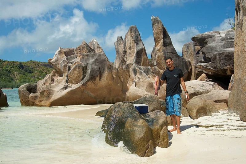 Seychelles island Curieuse with the famous granite rocks and man with caught fish