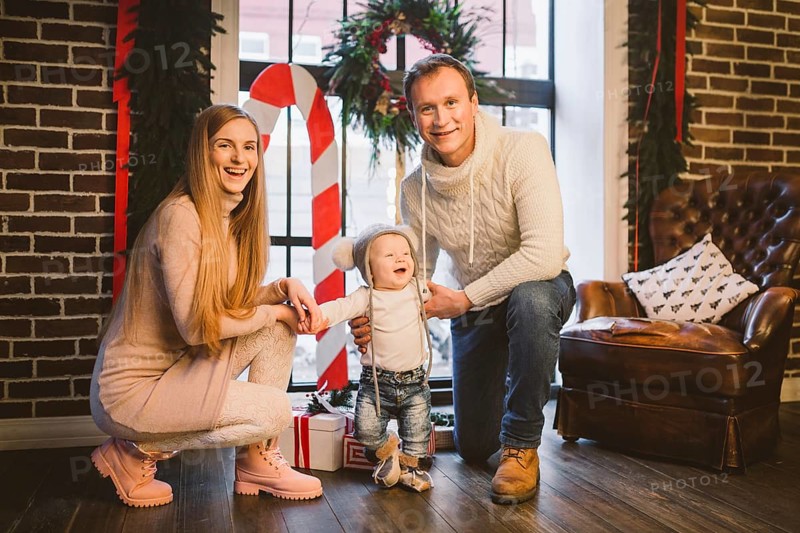 Theme of Christmas holidays and New Year mood. Family posing at home near christmas decor on christmas evening. Three mom dad and son in the winter at the window