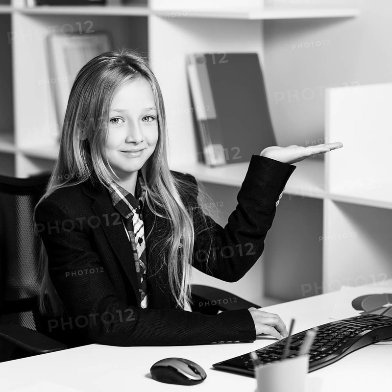 Little girl like business woman sitting at the desk with computer in blue office