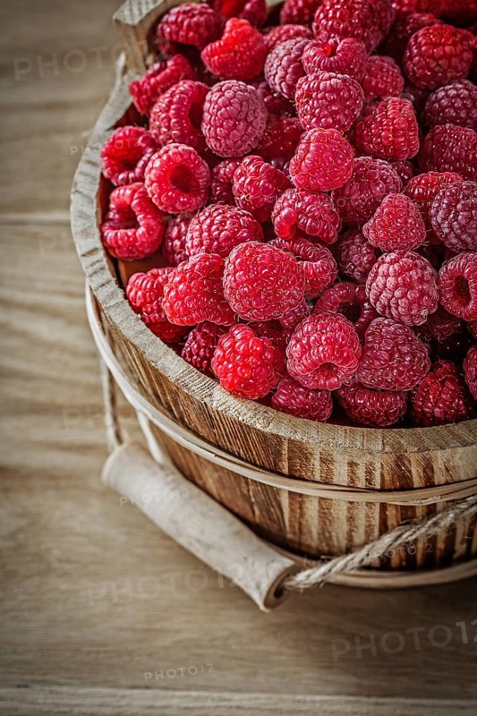 Ripe raspberries in bucket on wooden board