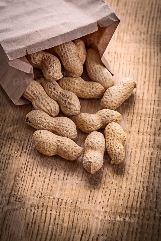 Peanuts poured from paper bag on wooden board food and drink still life