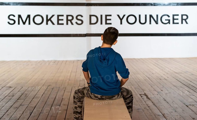 Teenager smoking and message on wall - Smokers die younger. No smoking concept with child. Casual clothes