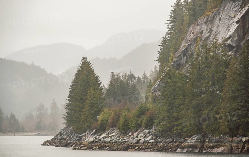 Misty forested mountains and rocky coastline bordering a calm body of water along the Sea to Sky Highway in British Columbia, Canada, North America
