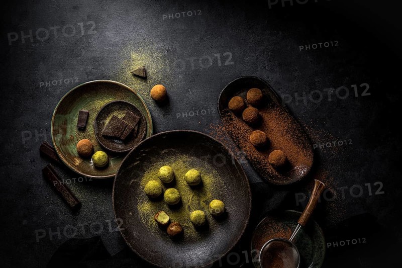 Overhead big plate with green truffle Matcha and plate with brown truffles balls with powder and strainer and chocolate pieces