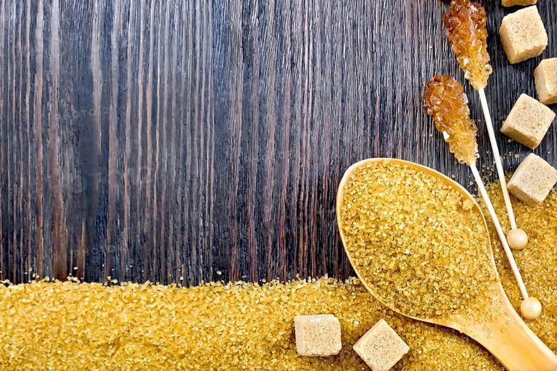 Sugar brown granules in a spoon, cubes and crystals on a stick in the form of a frame on the background of a wooden board