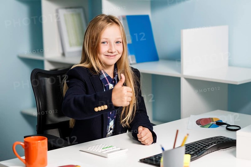 Little girl like business woman sitting at the desk with computer in blue office