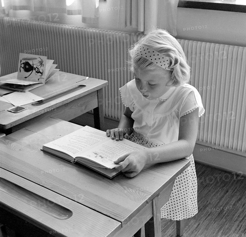 School in the 1950s. A girl is seen sitting at her desk in the classroom reading from the schoolbook in front of her. She is nicely dressed in a white skirt with a dotted pattern and matching headband. Sweden 1957 Conard ref 3538