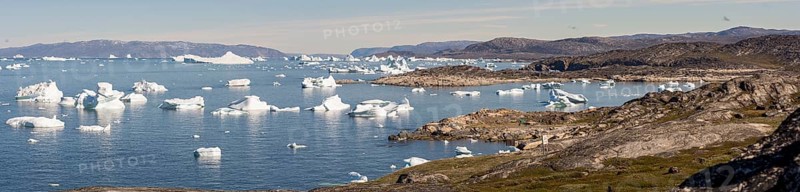 A breathtaking coastal landscape near Ilulissat, Greenland, featuring the Arctic Ocean dotted with massive icebergs. The rugged shoreline and icy waters create a serene yet dramatic scene, showcasing the pristine beauty of the Arctic wilderness, North America