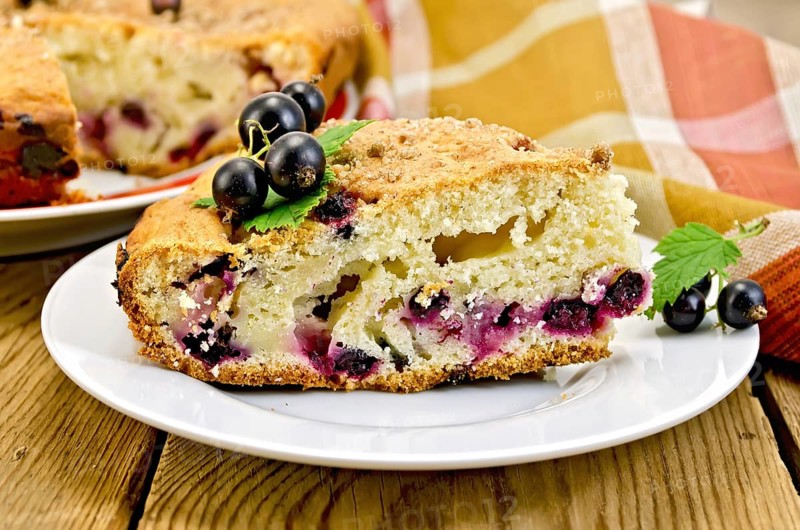 Sweet piece of cake with black currant on a plate, napkin on the background of wooden boards
