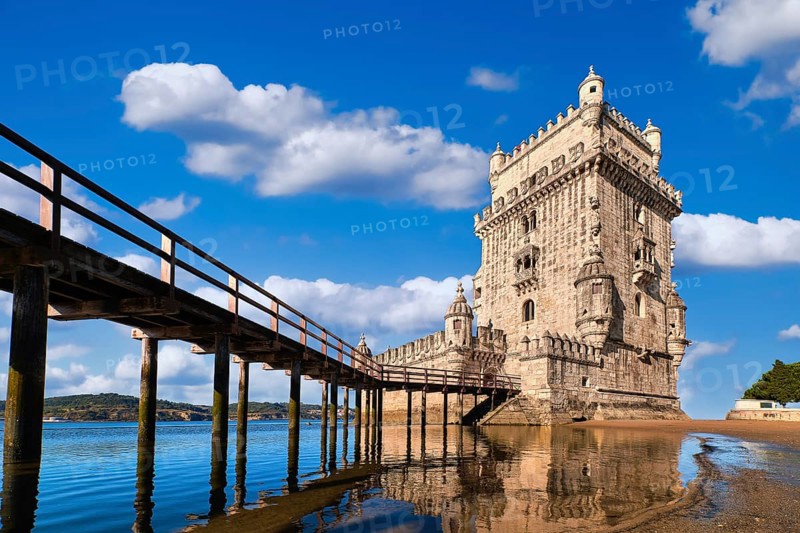 Belem tower and wooden bridge to it, Lisbon, Portugal at blue summer day sky with clouds. Medieval fort on Tagus river in late Gothic or Manueline style, UNESCO world heritage site, Age of Discoveries, tourist attraction, Portuguese seafaring history