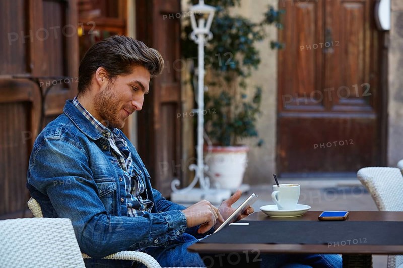 Young man with tablet pc touch in an cafe outdoor having some coffe cup