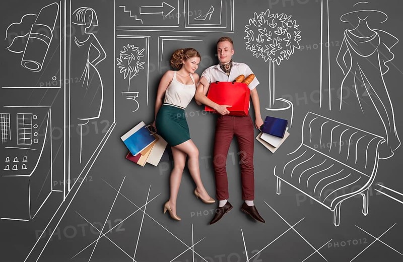 Love story concept of romantic couple shopping against chalk drawings background. Young happy couple standing together with shopping bags in a shopping centre