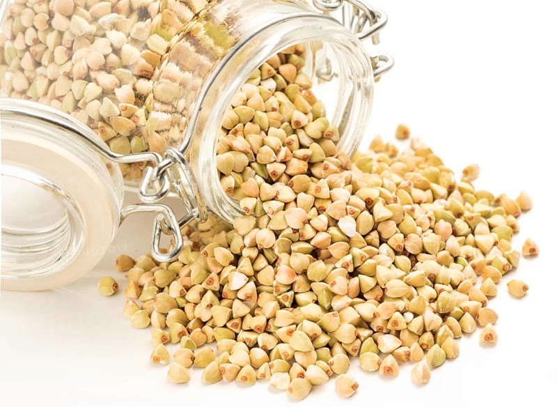 Raw green buckwheat in bank on white background