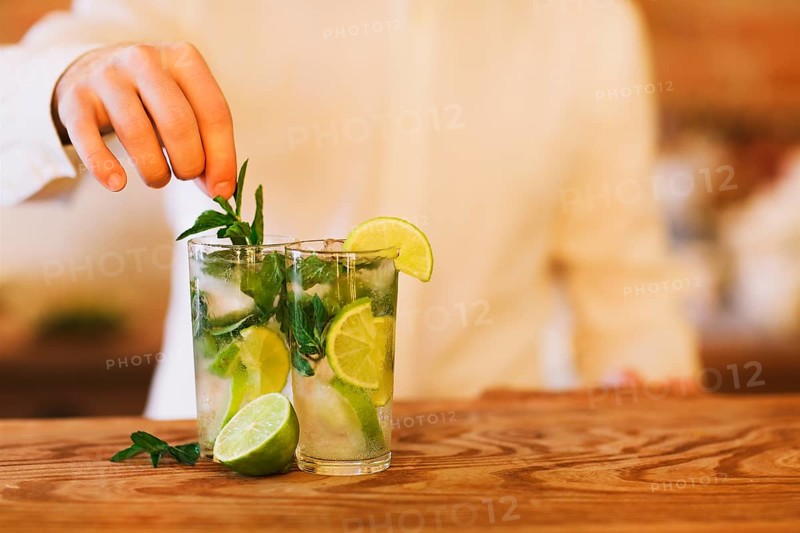 Bartender making two mojito cocktails on wooden bar counter