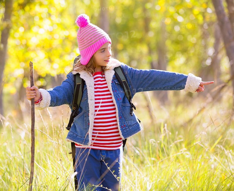 Hiking kid girl with backpack pointing finger in autum poplar trees forest