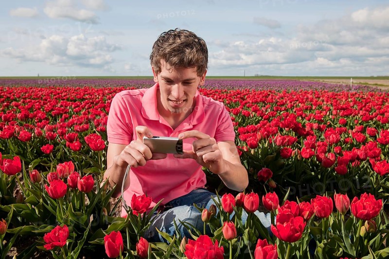 Portrait of an young man taking pictures in tulips field with photo camera