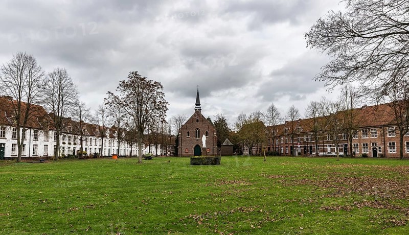 Belgium, 12 08 2018: Old houses and a chapel at the beguinage with bare trees and a meadow during winter, Europe