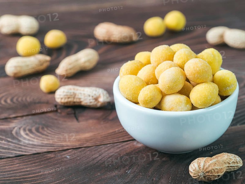 Peanut snack for beer, wine, party bar. Salted peanuts in yellow cheese glaze on brown wooden table. Copy space